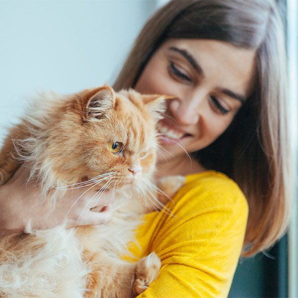 female smiling while holding fluffy orange cat